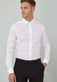 Hvid langærmet skjorte med knapper lavet af glat stof og spids krave, parret med sorte bukser, der har en strømlinet pasform og underspillet design.