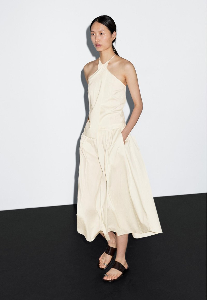 Woman in cream halter top and matching wide-leg pants standing on black and white floor wearing dark sandals.