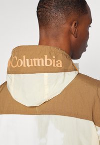 Brun og creme jakke med hætte, Columbia branding på kraven og tekstureret stof med kontrasterende sektioner.