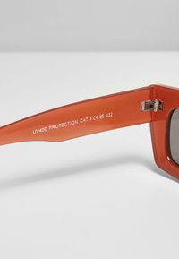 Oranžid plastmassprillid, millel on paks raam, hallid läätsed ning kaarel on graveeritud tekst, mis näitab UV400 kaitset ja kategooriat.