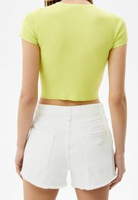 Ribbed lime green crop top dengan lengan pendek, dipadukan dengan celana pendek denim putih yang memiliki pinggiran robek dan saku belakang.