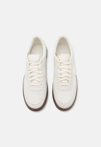 Weiße Wildledersneaker mit strukturiertem Finish, ausgestattet mit cremefarbenen Schnürsenkeln, einer gepolsterten Einlegesohle und einer braunen Gummisohle. Subtile Logoakzente.
