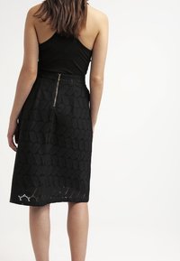 Zwarte knielange rok met een gestructureerd honingraatpatroon, voorzien van een verborgen rits aan de achterkant en een gladde stofafwerking.