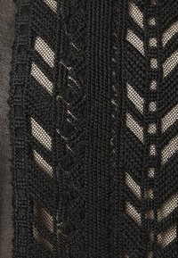 Tessuto nero a maglia con una intricata cucitura decorativa. Presenta un mix di texture tra sezioni a rete e sezioni solide, evidenziando forme geometriche.