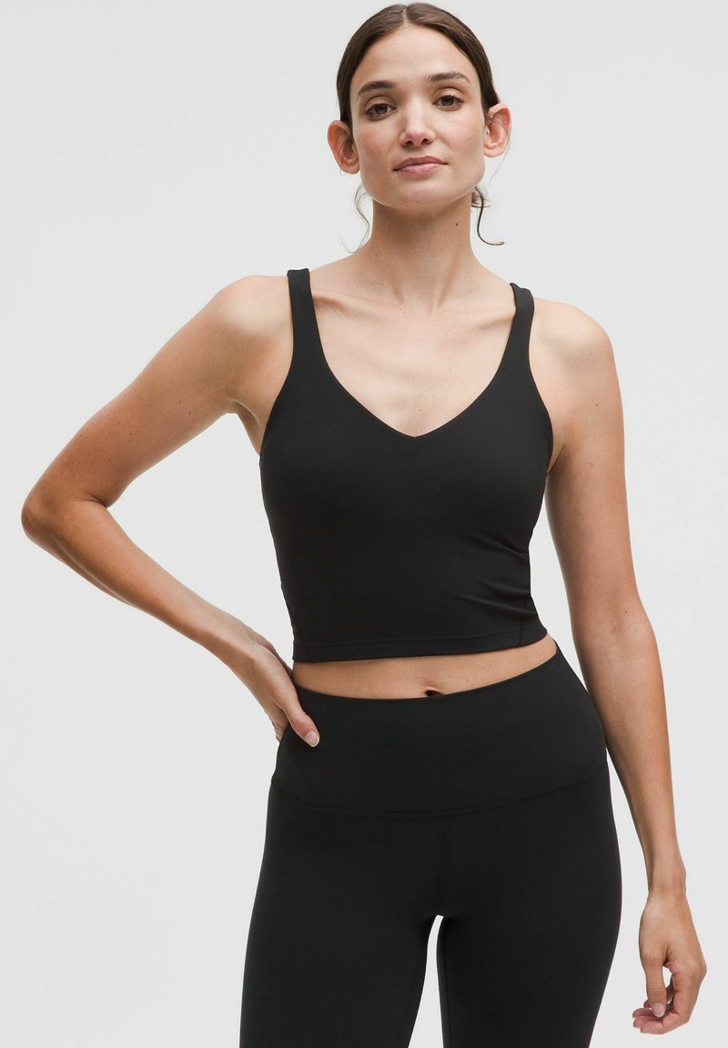 Black cropped sports bra with a V-neckline and wide straps, made of a smooth, stretchy material. Paired with high-waisted black leggings.