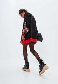 Maglione nero oversized con maniche a fantasia colorata e orlo rosso, abbinato a stivaletti neri in pelle verniciata con tacco spesso beige.