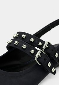 Μαύρα παπούτσια Mary Jane από σουέντ με δύο λουράκια διακοσμημένα με ασημένιες πυραμίδες και μεταλλικές αγκράφες. Κλειστή μύτη και σχέδιο με χαμηλό τακούνι.