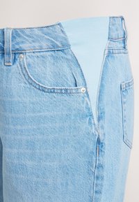 Lyseblå denimjeans med elastisk talje, der har en forlommer og en svag tekstur. Materialet virker holdbart og afslappet.