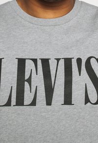 Camiseta de algodón gris con una gran impresión en negro y en bold que dice "LEVI'S". Diseño simple de cuello redondo con un acabado suave y texturizado.