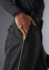 Pantalones softshell negros con un diseño ajustado, que cuentan con un bolsillo lateral con cremallera y ribete en amarillo neón, además de una cinturilla ajustable.