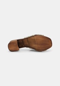Sabot à semelle en bois avec une base beige, présentant une texture lisse et des clous en métal doré le long de la lanière. Design à dos ouvert pour une meilleure ventilation.