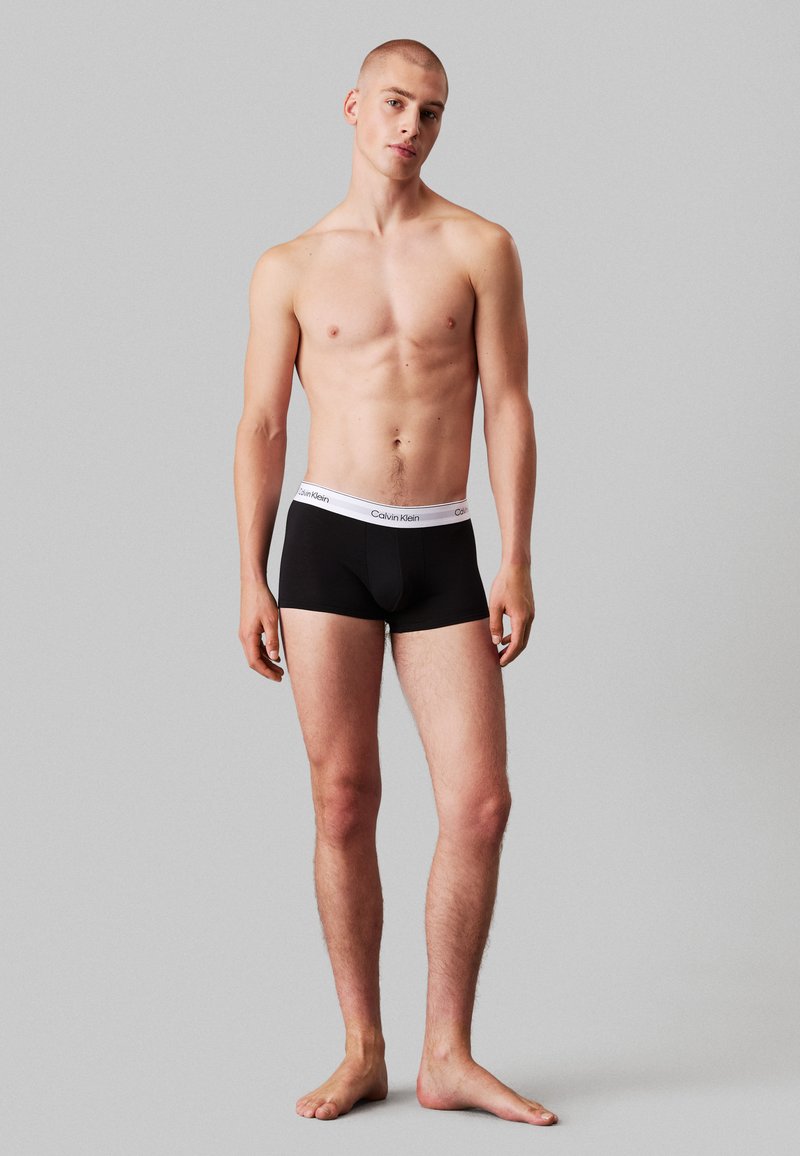 Schwarze trunk-artige Unterwäsche mit einem weißen Calvin Klein Logo-Gummibund. Glattes Material, enganliegendes Design und ohne Muster oder sichtbare Hardware.