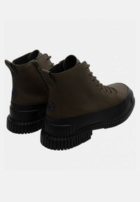 Botas altas marrones hechas de un material suave, con una gruesa suela de goma negra y un cierre lateral para un fácil acceso. Detalle del logo visible.