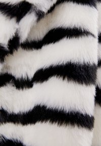 Umělá kožešina s výraznými černými a bílými pruhy různých šířek, s jemným, texturovaným povrchem.