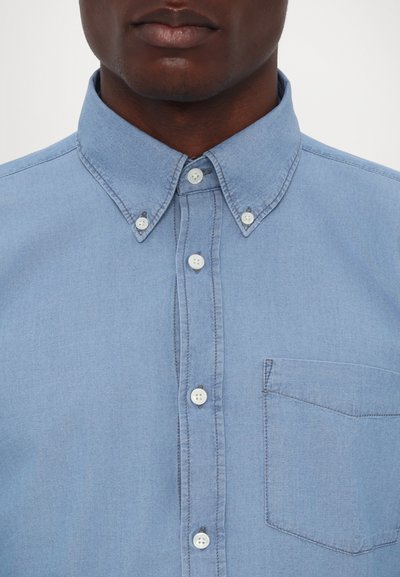 Light blue button-up shirt with a collar, featuring a chest pocket, white buttons, and visible stitching details. Cotton-like texture.