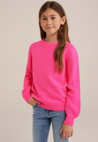 Heller pinker Strickpullover mit einem strukturierten Muster, Rundhalsausschnitt und gerippten Bündchen, kombiniert mit blauen Jeans.