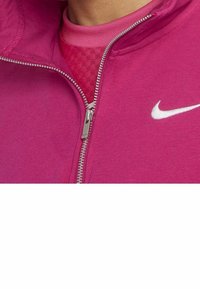 Rosa sportig zip-up jacka med en silverdragkedja, som har en vit logotyp på den övre vänstra sidan och ett texturerat innerlager.