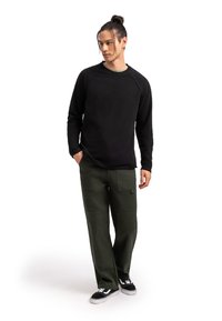 Felpa nera a maniche lunghe, pantaloni cargo verdi con tasche e sneakers nere. L'outfit presenta una vestibilità comoda e texture morbide.