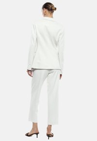Completo bianco su misura con giacca a scollatura a revers e pantaloni dritti. Realizzato in un tessuto liscio con dettagli di bottoni.