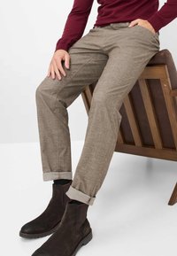 Beige maßgeschneiderte Hose aus strukturiertem Stoff, mit umgeschlagenen Säumen und flachem Vorderteil. Getragen mit dunklen Chelsea-Stiefeln und einem burgunderfarbenen Langarmshirt.