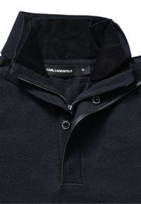 Navyblaues, strukturiertes Poloshirt mit Reißverschluss vorne, geripptem Kragen und Logo-Knöpfen, aus weichem Stoff. Größenetikett sichtbar.