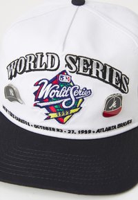 Bela bejzbol kapa s temnim pomolom, ki ima napis "SVETOVNO PRVENSTVO" ter barvite vezenine in dva logotipa: New York Yankees in Atlanta Braves.