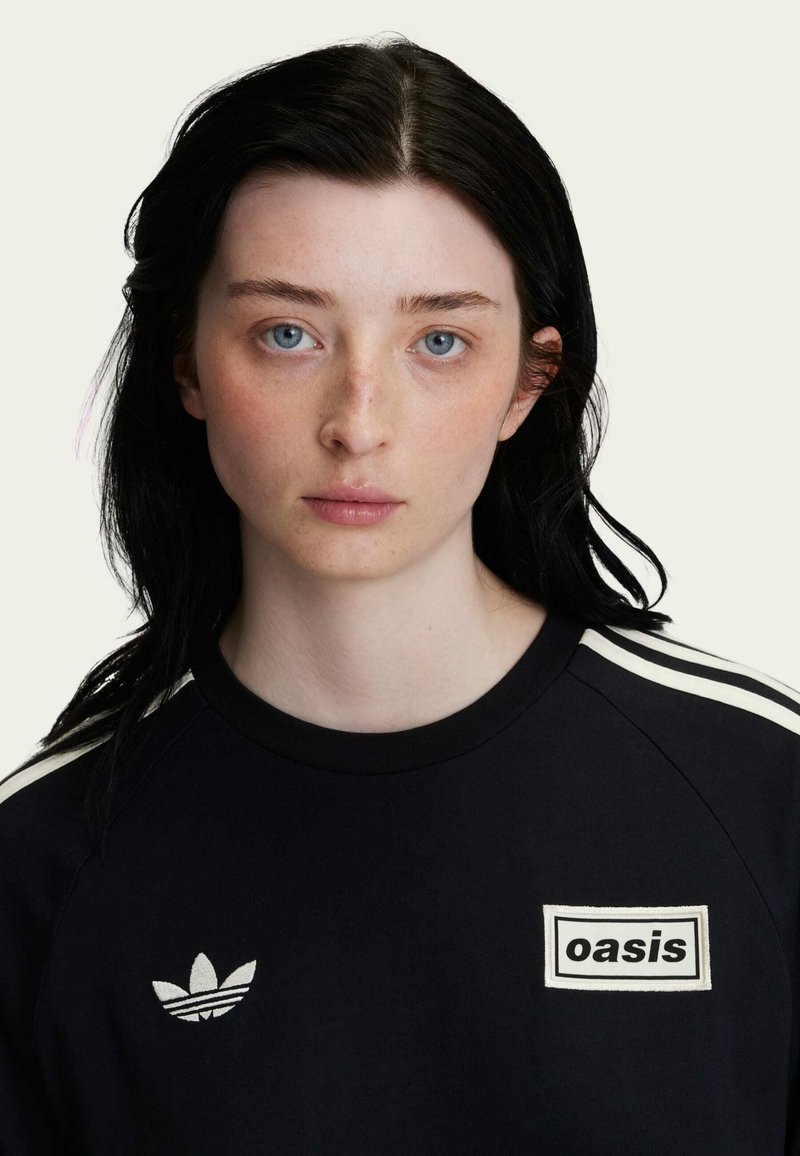 Black short-sleeve sweatshirt featuring white striped accents, a rounded neckline, and a square "oasis" logo patch on the front.
