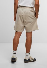 Beige Baumwollshorts mit einem elastischen Bund, seitlichen und hinteren Taschen sowie einem lockeren Schnitt, kombiniert mit schwarz-weißen gestreiften Socken und Sneakers.