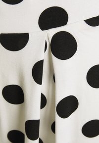 Pois noirs sur un tissu blanc avec une texture côtelée. Les plis accentuent le design, créant un effet visuel dynamique.