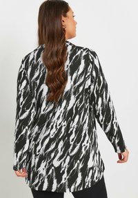 Blusa a maniche lunghe bianca e nera con un tessuto testurizzato caratterizzato da un motivo astratto ondulato, leggermente più lunga sul retro.