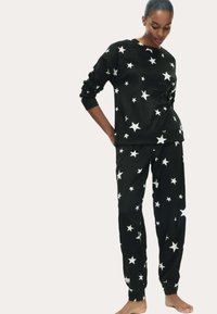 Zwarte fleece pyjama's met witte sterrenpatronen. De top heeft een ronde halslijn en lange mouwen; de broek heeft een elastische taille en ribgebreide boorden.