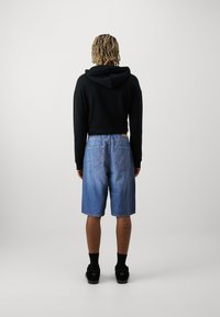 Sudadera con capucha negra y pantalones cortos de mezclilla azul de corte relajado, con bolsillos traseros y dobladillo recto, combinados con calcetines y zapatos negros.