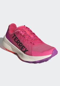 Růžová běžecká bota s prodyšným svrškem, černým logem "TERREX", texturovanou mezipodešví a vícero barevnou podešví s růžovými, fialovými a oranžovými akcenty.
