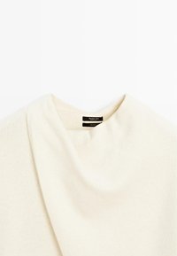 Light beige sweater made of 100% wool. Features a draped neckline and smooth texture. Label positioned near the collar.