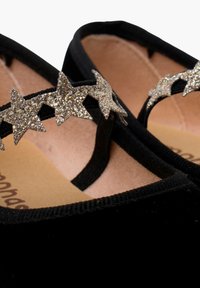 Schwarze Samt-Ballettschuhe mit einem sternförmigen, glitzernden Riemen. Weiches Innenleben mit einer beigen Innensohle und strukturiertem schwarzen Rand.