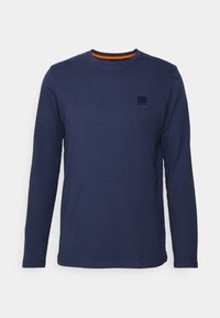 Maglietta a maniche lunghe blu navy in cotone, con scollo rotondo e piccolo logo patch sul petto sinistro. Colletto a coste con accento arancione.