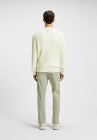 Maglione giallo chiaro a costine con una vestibilità rilassata, abbinato a pantaloni verde chiaro e scarpe beige, visto da dietro.