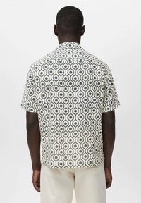 Camisa de manga corta en tela crema con un patrón geométrico en marino. Cuenta con un cuello y un dobladillo recto. La textura parece ligera y transpirable.