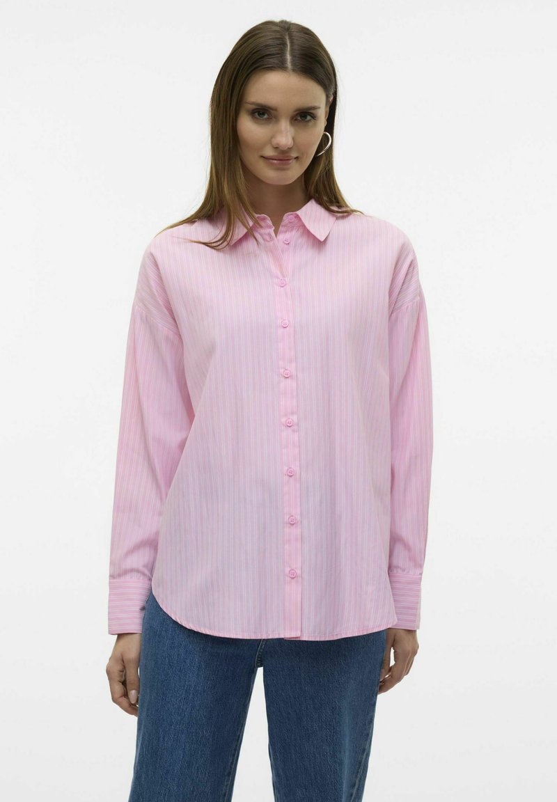 Lichtroze button-up shirt met dunne verticale strepen, ontspannen pasvorm, lange mouwen en een klassieke kraag. Gecombineerd met blauwe spijkerbroek.