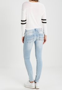 Ljusblå slim fit-jeans med en urtvättad textur, med en klassisk femficksdesign och en midjehöjd som är mitt emellan, ihop med en vit topp.