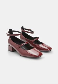 Red patent leather Mary Jane shoes with a square toe, ankle strap, and low block heel. The interior features a black lining.