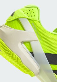 B baskets de sport jaunes vif avec une tige en maille, des accents texturés et une semelle blanche légère avec une rayure noire.