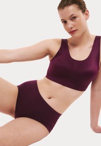 Burgundská sportovní podprsenka a vysoké šortky, vyrobené z hladkého a pružného materiálu. Nabízí jednoduchý design s širokými ramínky a bezšvovým provedením.