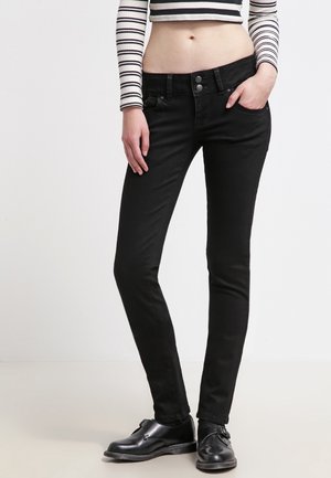 Jeans ajustados negros con una textura suave, cintura alta, dos botones frontales, trabillas para cinturón y diseño de cinco bolsillos. Combinados con zapatos negros.