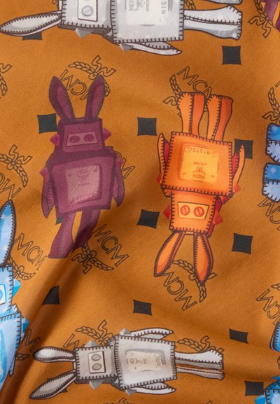 Καφέ ύφασμα με καρικατουρίστικες φιγούρες κουνελιών σε μωβ, πορτοκαλί και μπλε, με τετράγωνα διακοσμητικά και μοτίβα λογότυπου «MCM».