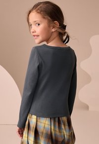 Top a maniche lunghe, a coste, di colore grigio scuro con scollo rotondo, abbinato a una gonna a quadri con colori giallo, blu e marrone.