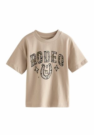 Beige Baumwoll-T-Shirt mit kurzen Ärmeln, auf dem "RODEO" in schwarzer Schrift, ein Hufeisendesign und Sternakzente abgebildet sind. Weicher Stoff, lockere Passform.