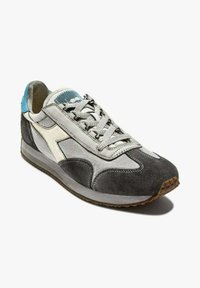 Sneaker grigia e bianca con materiali in suede e mesh, caratterizzata da un design testurizzato, chiusura con lacci e suola in gomma con accenti color gomma.