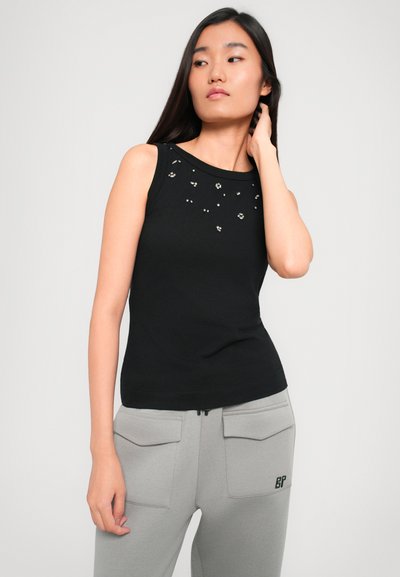 Fekete ujjatlan felső kerek nyakkal, az elején szétszórt strasszokkal. Világosszürke, zsebes melegítőnadrággal párosítva.