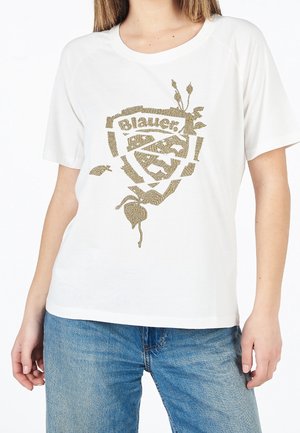T-shirt blanc à manches courtes avec motif de bouclier à points dorés et texte "Blauer", porté avec un jean bleu sur une personne sur fond blanc.